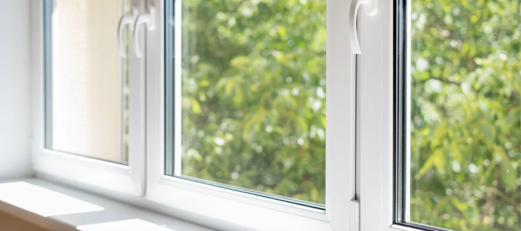 A close-up view of a three-pane white window looks out onto lush green trees